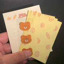 Load image into Gallery viewer, A hand holding a stack of small yellow sticky notes decorated with cute teddy bear illustrations and bread patterns, set against a dark desk background.