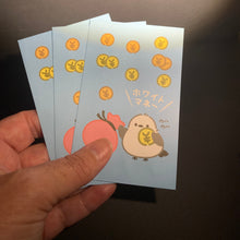 Load image into Gallery viewer, A hand holding a stack of light blue Japanese fortune stickers decorated with gold coins and a cute cartoon bird character, set against a dark background.