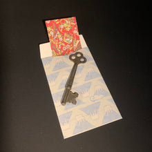 Load image into Gallery viewer, A vintage-style metal key displayed on mt. fuji patterned envelope with a red floral card peeking out, photographed on a dark background.