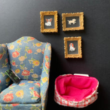 Load image into Gallery viewer, Three miniature framed pet portraits with gold frames and black backgrounds are arranged on a dark surface next to a small floral fabric pouch and a pink-lined zippered case.