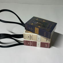 Load image into Gallery viewer, Bookworm's Holiday Ornament. The ornament is an open book; there's space to write a special message or add a personal touch. It's a perfect addition to your holiday decor, especially for book lovers and literary enthusiasts.
