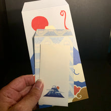 Load image into Gallery viewer, A hand holds a small cream-colored card featuring a blue mountain and red sun design, with two larger matching patterned envelopes behind it on a dark background.