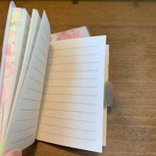 Load image into Gallery viewer, A small, kawaii-style notebook with a soft cover featuring an illustrated cherry blossom scene, a cat with a red ribbon, a bicycle, and a vending machine. The notebook measures 4.25 x 3 in, has 70 lined pages, and secures with a velcro close.