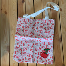 Load image into Gallery viewer, Cream canvas Kawaii cherry tote bag with embroidered red and pink cherries and purple bows, featuring a foldable and portable design for shopping, measuring 15.9 inches x 14.6 inches with 9.8 inches handle height, Shown on wood table.