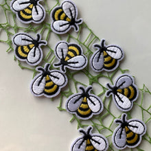 Load image into Gallery viewer, Embroidered bumble bee iron-on patches with bright yellow and black stripes and white wings, displayed on a lacey green cloth.