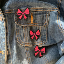 Load image into Gallery viewer, Application demo: Pink bow patches being applied to denim jacket .