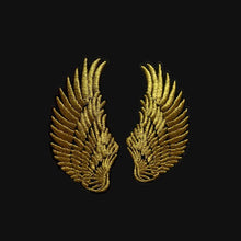 Load image into Gallery viewer, Gold wing-shaped patches held by a hand on a gray background