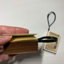 Load image into Gallery viewer, A close-up view of the Bookworm's Holiday Ornament. The ornament is an open book; there's space to write a special message or add a personal touch. It's a perfect addition to your holiday decor, especially for book lovers and literary enthusiasts.
