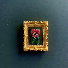 Load image into Gallery viewer, Decorative heart with a face and green bow in a gold frame on a dark background
