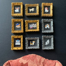 Load image into Gallery viewer, Nine miniature framed art pieces, each depicting a small dog illustration inside an ornate gold or silver frame, arranged in a 3x3 grid on a dark surface next to a dusty pink fabric.
