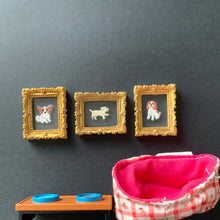 Load image into Gallery viewer, Three miniature gold-framed dog portrait pins are arranged vertically next to a small pink and white gingham fabric pouch with a bright pink interior, on a dark gray background.
