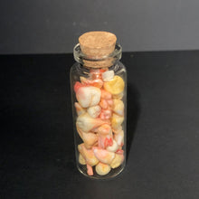 Load image into Gallery viewer, A small clear glass bottle with a cork stopper, filled with small sculpted prop teeth in pastel cream, pink, and yellow tones, set against a dark gray background.
