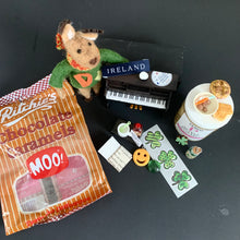 Load image into Gallery viewer, Reindeer character in a green scarf seated beside a miniature upright piano marked with an Ireland decal

