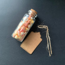 Load image into Gallery viewer, A small clear glass bottle with a cork stopper filled with stained and bloody faux prop teeth, placed on a dark surface beside a blank kraft paper tag and twine.
