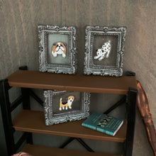 Load image into Gallery viewer, Three ornate silver frames displaying painted dog illustrations, arranged on and beside a brown wooden shelf against a textured gray wall.
