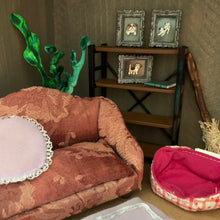 Load image into Gallery viewer, A dollhouse miniature room scene featuring a patterned pink and brown armchair, a small wooden shelf with three framed animal portraits, a green plant, and a pink-and-white checkered hat on a cardboard backing.
