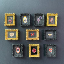Load image into Gallery viewer, ten miniature framed art pieces arranged in a 3x3 grid on a dark gray background. The frames alternate between ornate gold and black styles, each containing a small, detailed illustration such as a heart, flower, butterfly, and snake.
