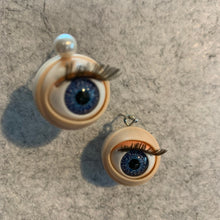 Load image into Gallery viewer, Blinking Eyeball-shaped earrings supplies with blue eyes and and brown lash details on a gray surface
