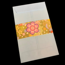 Load image into Gallery viewer, A blue envelope featuring a decorative paper band wrapped around the middle, printed with a retro floral pattern in yellow, pink, orange, and purple, set against a solid black background.
