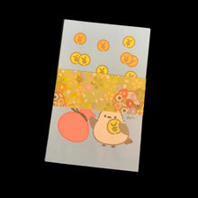 Load image into Gallery viewer, A small rectangular card or notebook with a Japanese-style illustration, featuring a bird holding a gold coin, a peach-colored plum blossom, and several gold coin motifs on a pale blue background, placed on a dark brown surface.
