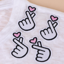 Load image into Gallery viewer, Four white embroidered Korean finger heart patches with pink hearts arranged on a white tee shirt.
