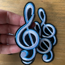 Load image into Gallery viewer, Large black and white embroidered treble clef iron-on patch in white, blue, and black, measuring 3.7 inches x 1.6 inches. Displayed on a wood surface.

