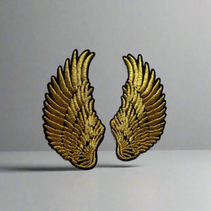 Gold wing-shaped patches held by a hand on a gray background