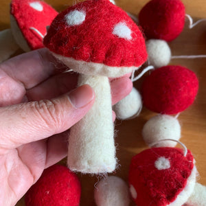 Close-up of a 72-inch garland featuring needle-felted red and white mushroom shapes and felt balls, made with wool and cotton fibers.