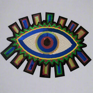 Large 12 inch rainbow sequin Evil Eye patch with vibrant colors and radiant rays, displayed on a wood table to display bold statement accessory.