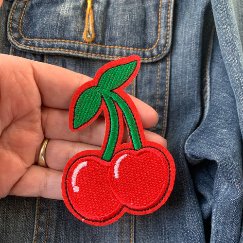 Close-up of embroidered red cherry iron-on patch, pictured against a denim jacket.