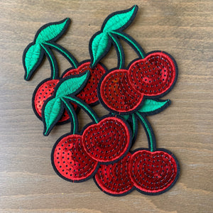 Embroidered Sequin Cherry Iron-On Patches on a wood table.