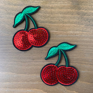 Two Sequin Cherry Patch with Embroidered Leaves shown on a wood table.