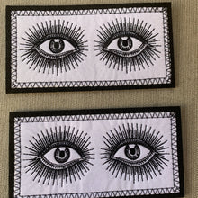 Load image into Gallery viewer, Embroidered Black and White Rectangle Vintage-look eyes iron-on patch, close-up on beige fabric background.

