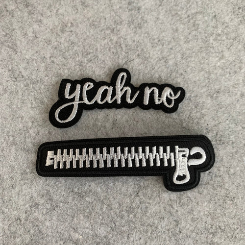 Two black and white patches with yeah no text and zipper embroidery on a gray surface