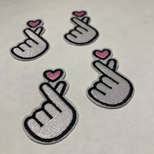 Load image into Gallery viewer, Four white embroidered Korean finger heart patches with pink hearts arranged on a white tee shirt.
