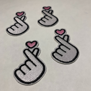 Four white embroidered Korean finger heart patches with pink hearts arranged on a white tee shirt.