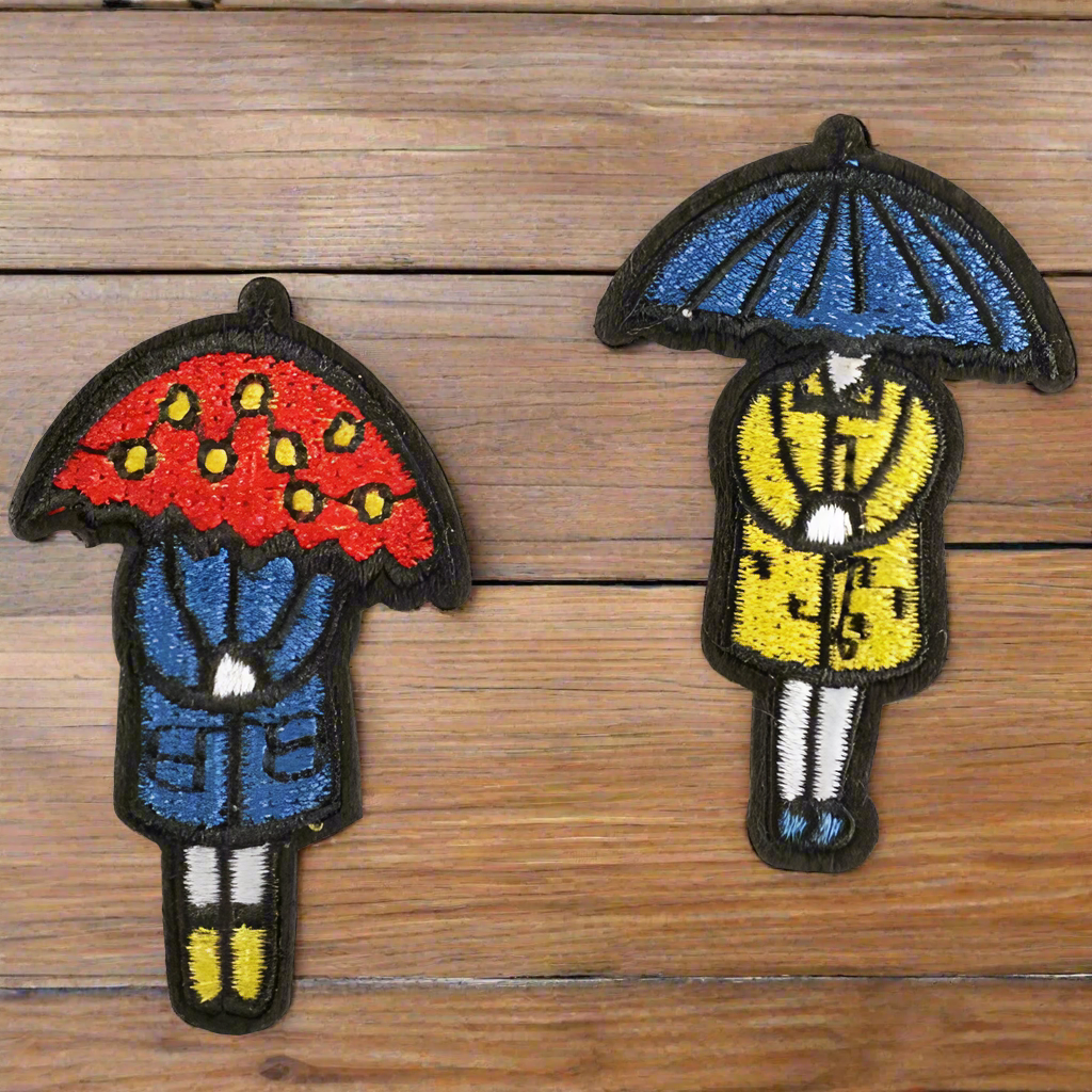 girl in raincoat under umbrella patch set. Red, blue, yellow embroidered PNW Seattle Rain Iron on patch set on wood table.